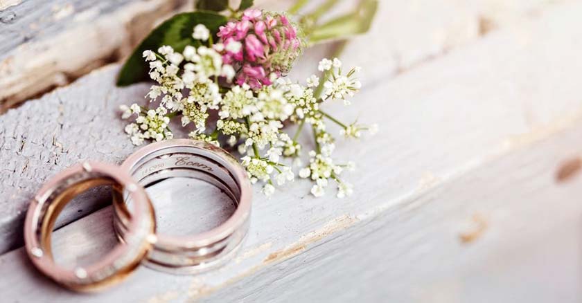 anillos de matrimonio sobre mesa de madera al lado de flores