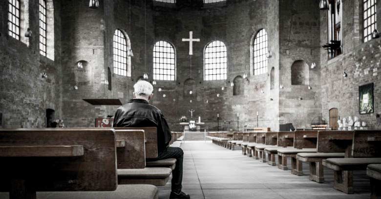 hombre en oracion sentado iglesia rezando bancos luz tenue 