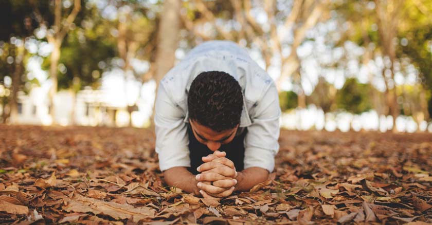 hombre rezando arrodillado sobre hojas caidas de un arbol