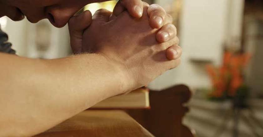 hombre rezando en oracion con las manos juntas en la banca de una iglesia 