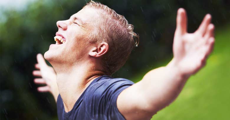 joven hombre muy contento brazos abiertos bajo la lluvia 