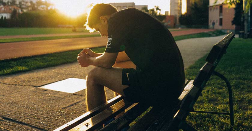 joven sentando en una banca solo triste deprimido puesta de sol