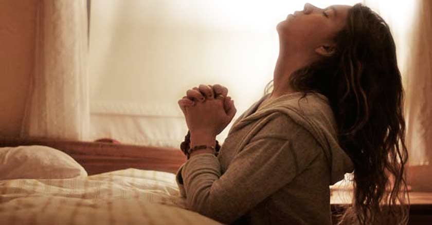 mujer arrodillada al pie de la cama con ojos cerrados orando en oracion