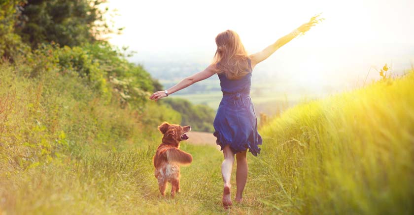 mujer caminando feliz al lado de su perro por verdes praderas