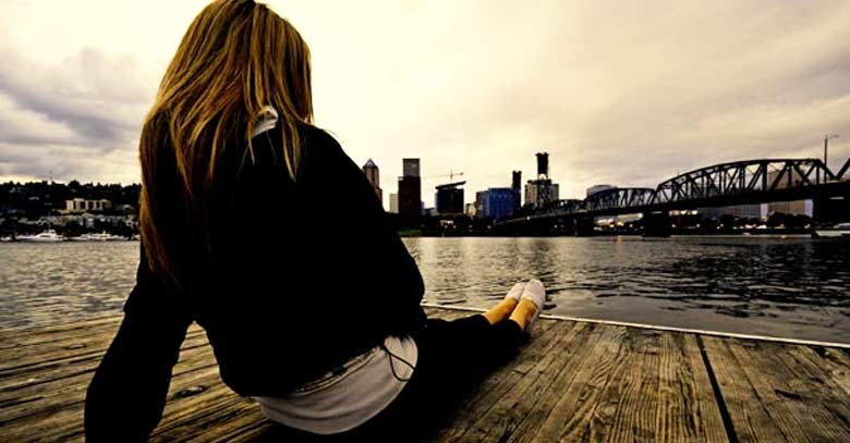 mujer recostada en un muelle mirando mar barcos