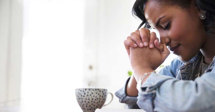 mujer rezando orando con las manos juntas y ojos cerrados en la mesa taza de cafe