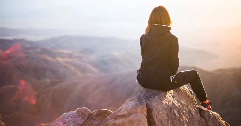 mujer sentada en la cima de una montana viendo el horizonte ocaso sol