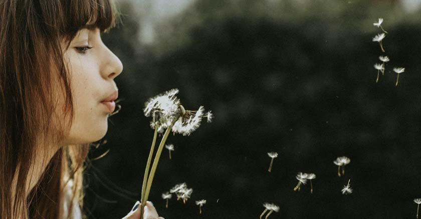 mujer soplando una flor en el bosque fondo arboles oscuros