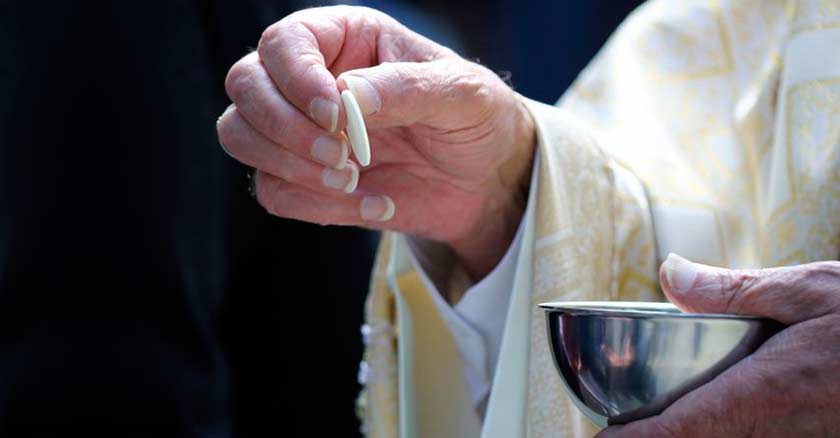 sacerdote tomando una hostia con su mano de la patena para dar comunion caliz