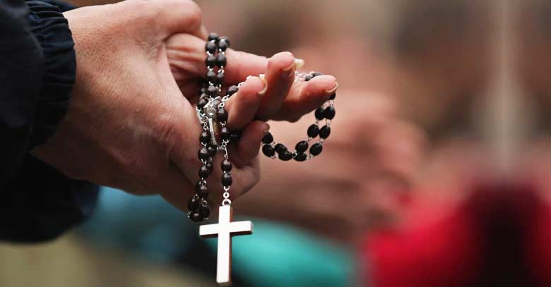 sosteniendo rosario color negro en mano rezando