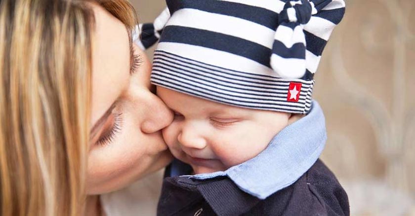 madre besando a su bebe en la mejilla bebe con gorro