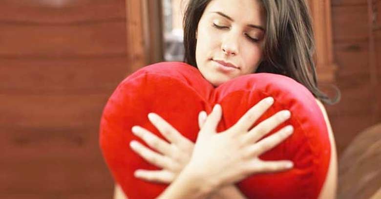 mujer abrazando almohada con forma de corazon rojo amor