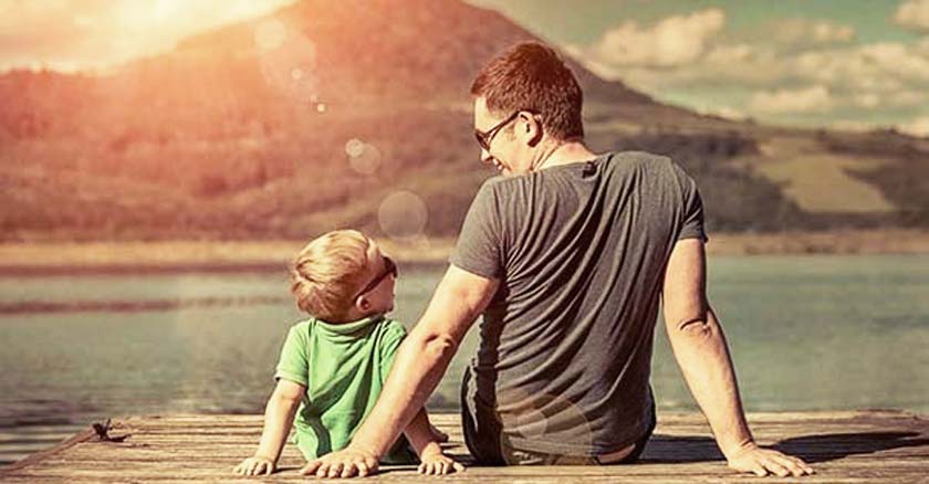 papa e hijo sentados en un muelle viendo el lago y sonriendo