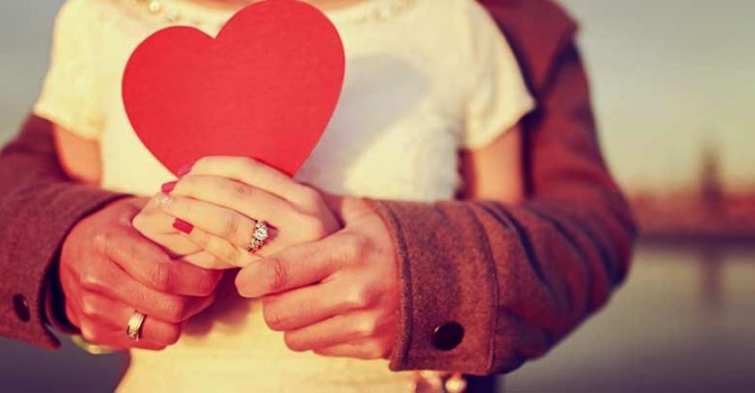 pareja de esposos sosteniendo un corazon rojo esposo abraza esposa desde atras dia