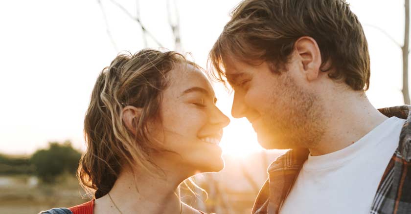 pareja de novios esposos muy cerca sonrien casi se besan luz de ocaso sol fondo