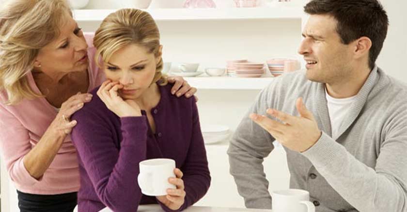 suegra diciendo algo al oido a su hija esposa frente al esposo