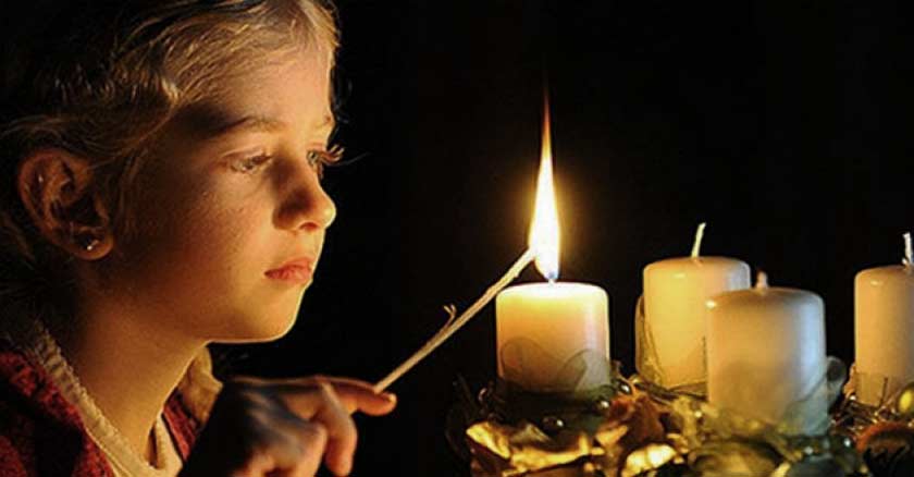 una chica tomando un encendedor encendiendo velas de adviento corona