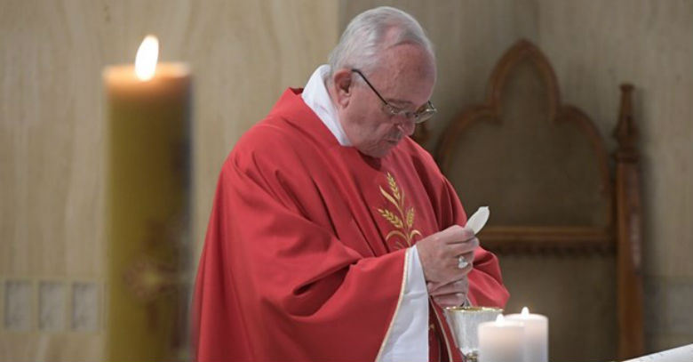 papa francisco sostiene hostia consagrada santa misa vestido rojo altar velas 