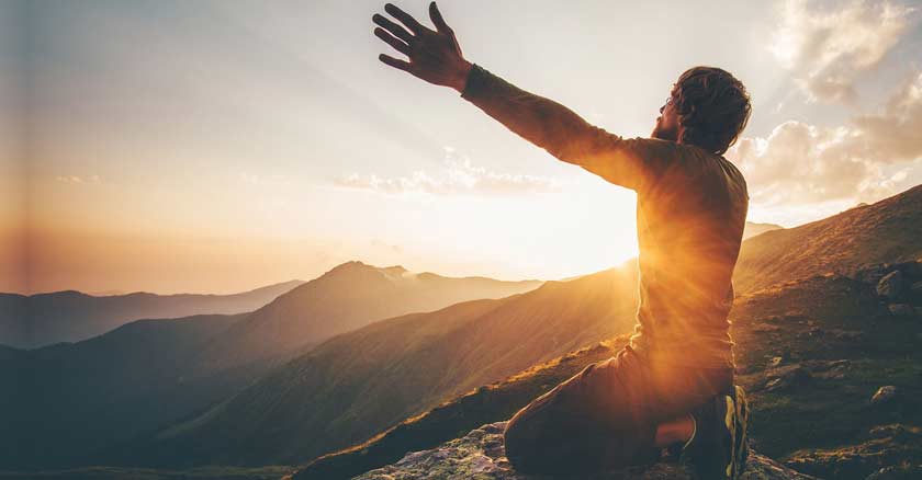 hombre arrodillado levantando sus brazos al cielo orando luz del sol ocaso