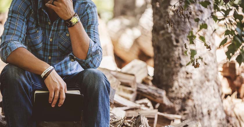 hombre sentado en la raiz de un arbol biblia en mano