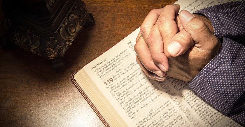 manos de hombre juntas orando sobre la santa biblia