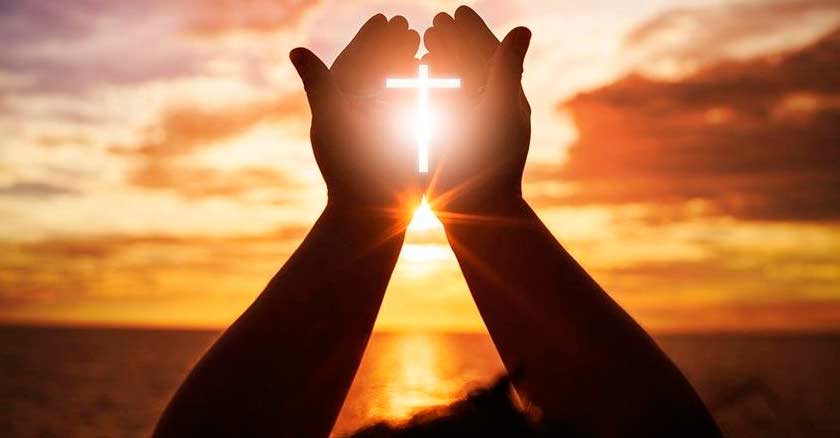 manos en oracion fomando una cruz con reflejo de sol atardecer orar cesar perseverante