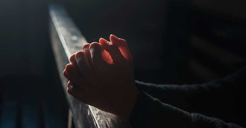 manos orando juntas en la oscuridad en iglesia asientos