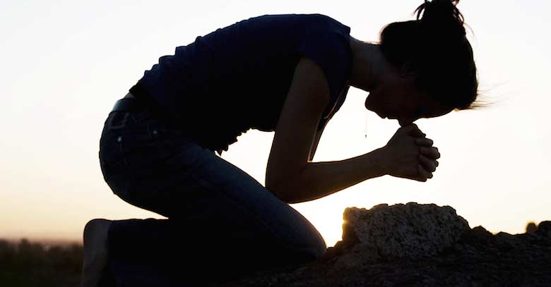 mujer arrodillada orando en piedras