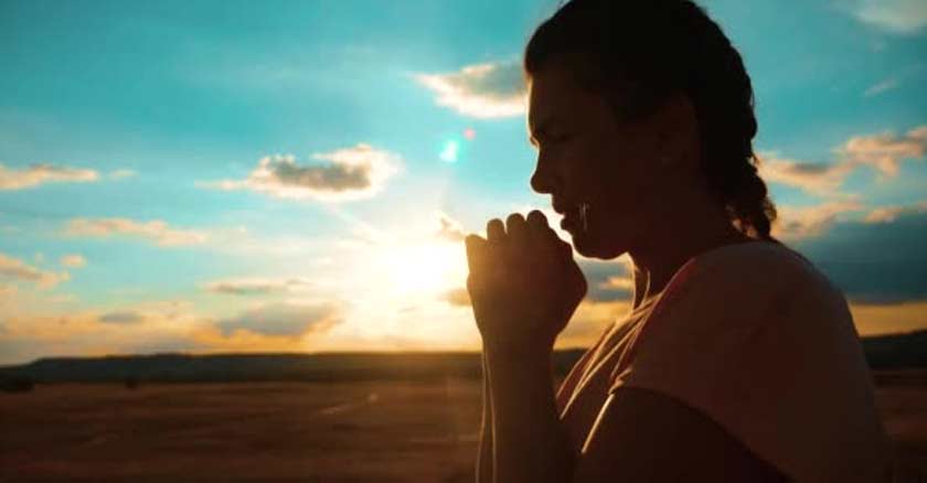 mujer orando en oracion con las manos juntas fondo cielo desierto arena