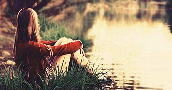 mujer sentada de espalda orillas del rio viendo atardecer