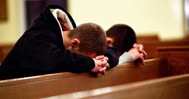  jovenes orando de rodillas en misa suplica