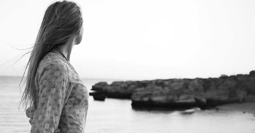 mujer en la orilla del mar viendo hacia el horizonte piedras 